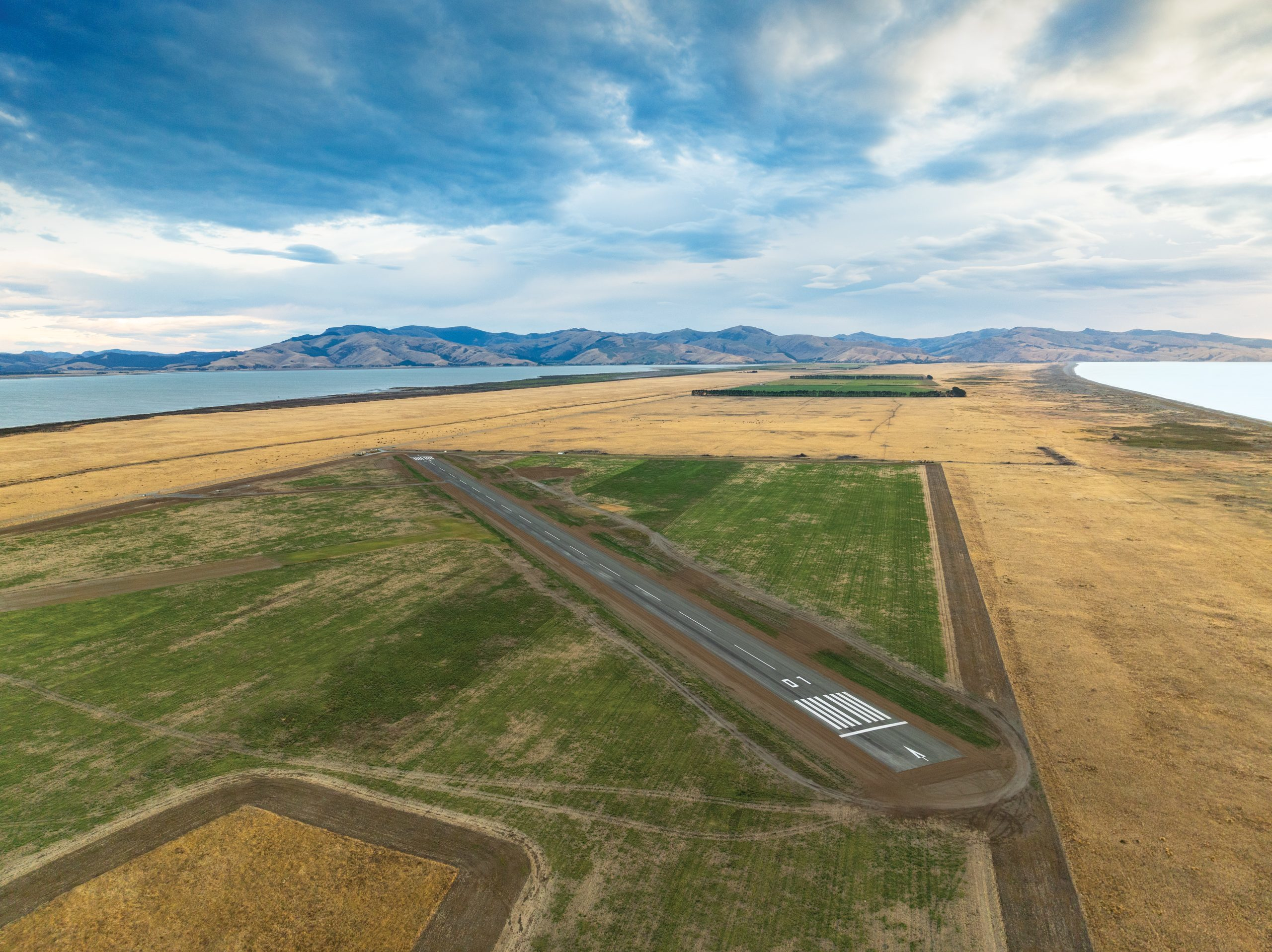 An aerial photograph of Tāwhaki's 01 runway looking along Kaitorete with Te Waihora | Lake Ellesmere and the Pacific Ocean.